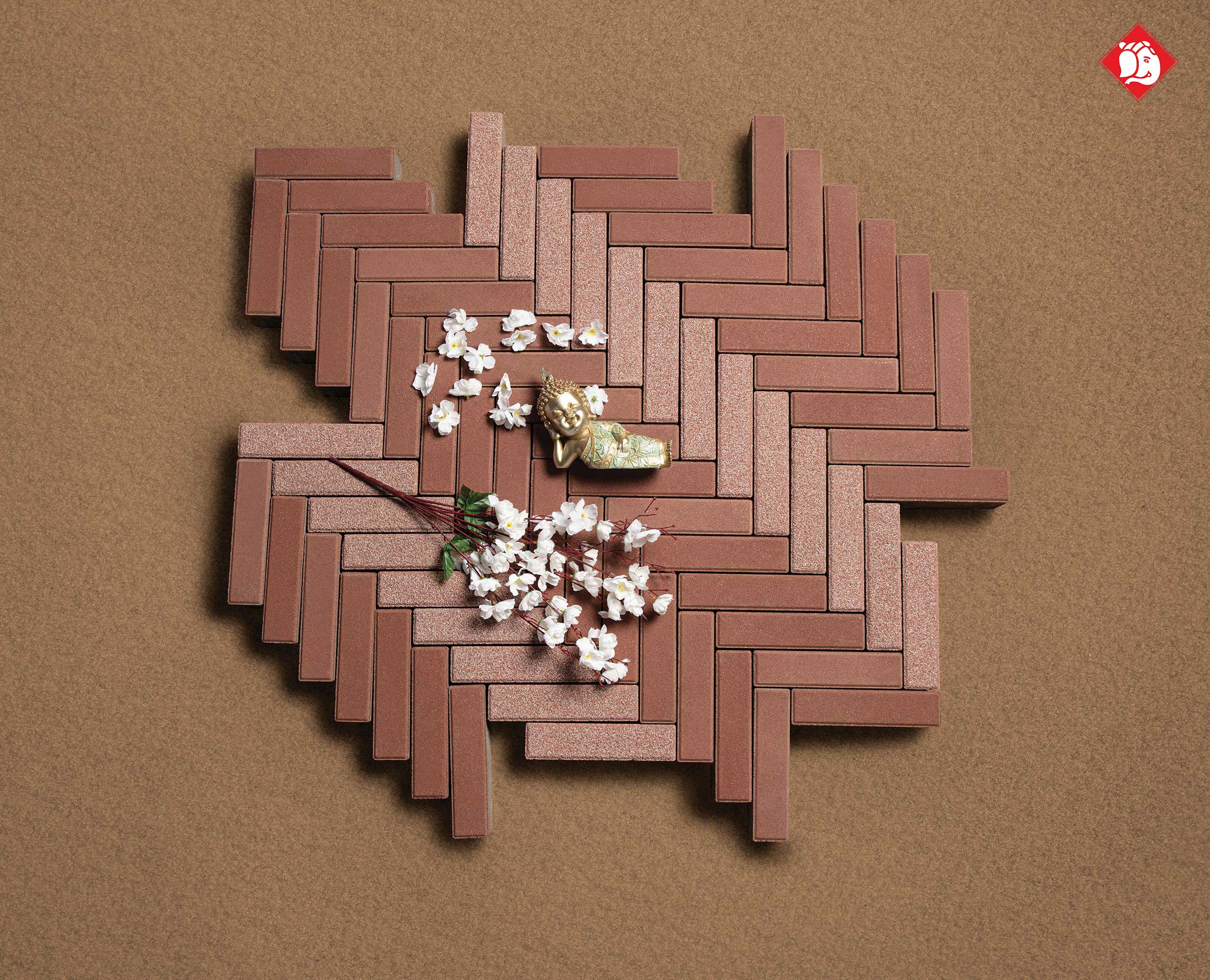 Vinayak Sanitarywares & Tiles: Brown herringbone tiles with white flowers and a small golden Buddha on a sand background