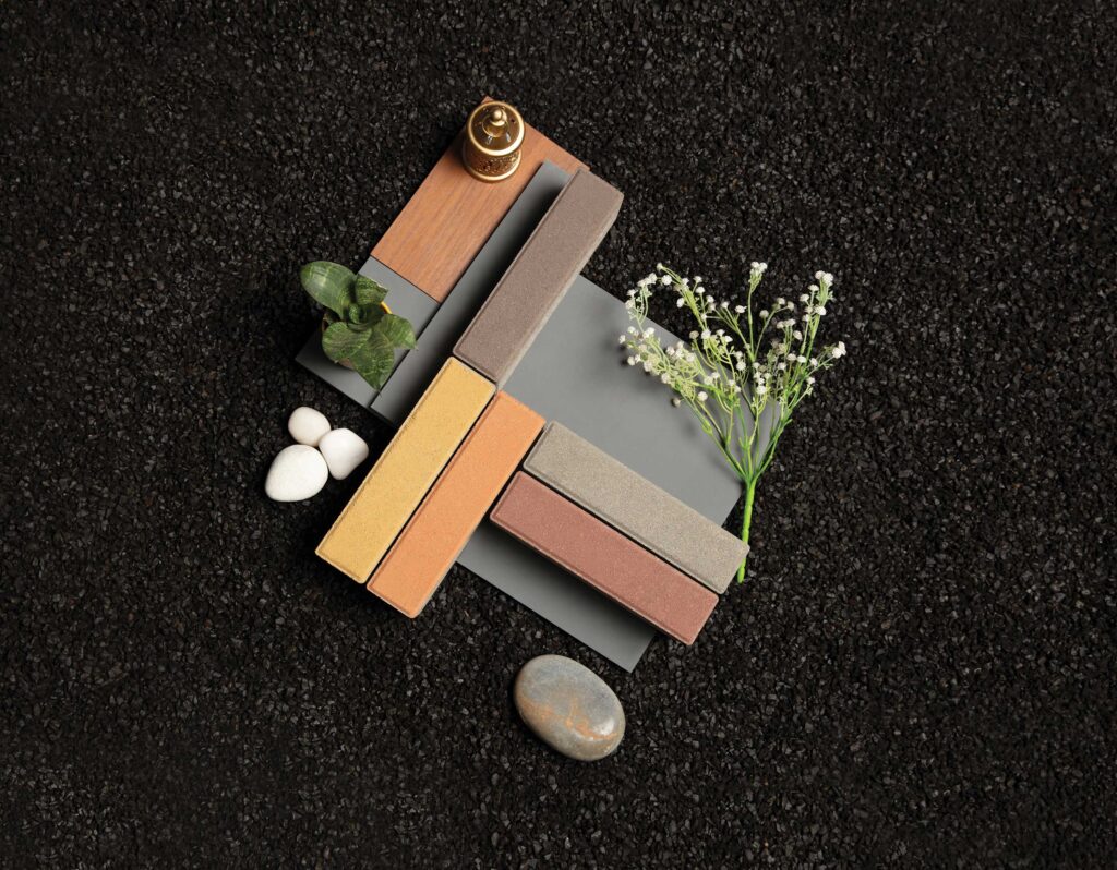 Vinayak Sanitarywares & Tiles: Rectangular tile samples in yellow, pink, brown and grey with white flowers, white stones and a brass bell on black
